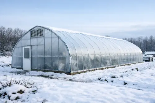 Snow-covered hoop house greenhouse wrapped in plastic film on a cold winter day