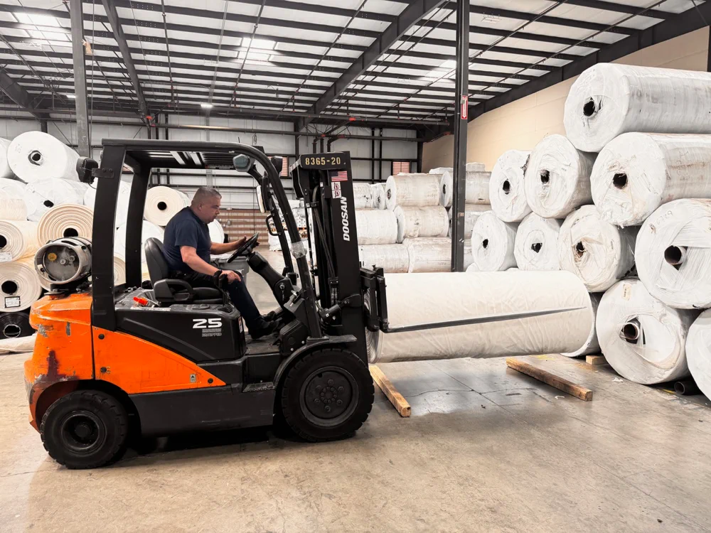 Forklift moving a full greenhouse plastic master roll inside a warehouse